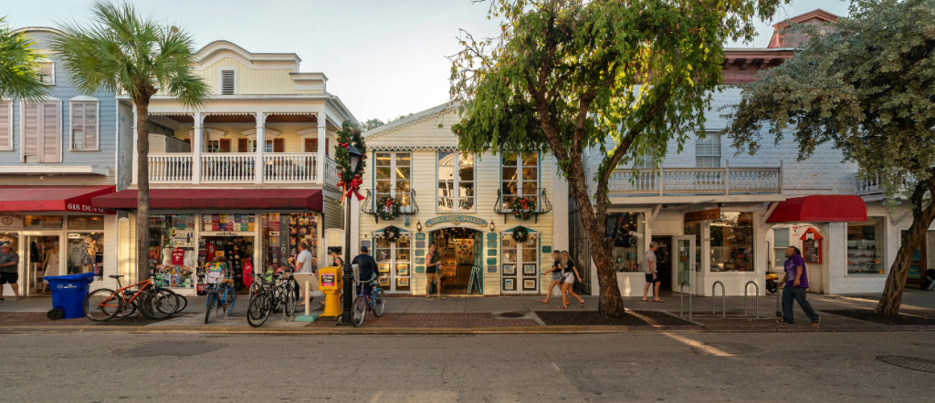 Duval Street in Key West, Florida, with colorful storefronts, palm trees, and pedestrians on a sunny evening