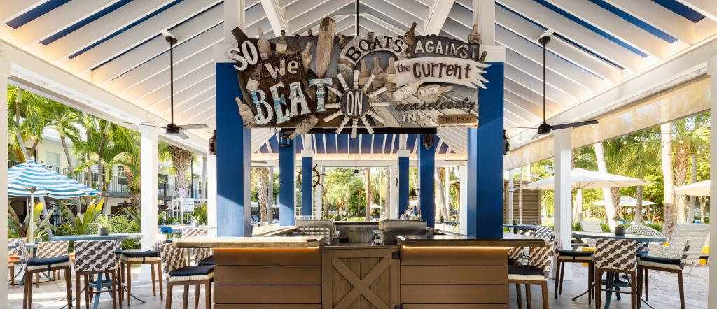 Rum Row poolside tiki bar at Blue Flamingo Key West, open-air bar with tropical palms, woven bar stools, and a vaulted blue and white pavilion. Pull up a stool at Rum Row, Blue Flamingo Key West's poolside tiki bar — your go-to spot for frozen cocktails, rum drinks, and all-day sunshine steps from the pool.