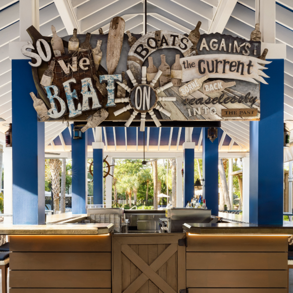 Rum Row poolside tiki bar at Blue Flamingo Key West, open-air bar with tropical palms, woven bar stools, and a vaulted blue and white pavilion