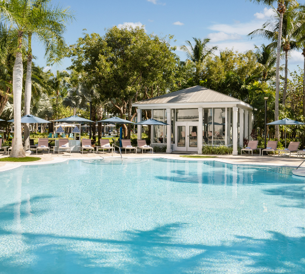 resort pool at Blue Flamingo Key West surrounded by palm trees, lounge chairs, blue umbrellas, and a glass-walled fitness center