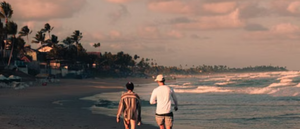 A couple walking together along a tropical beach beneath a colorful sunset sky