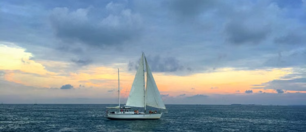A sailboat crossing calm blue water beneath a dramatic sky in Key West