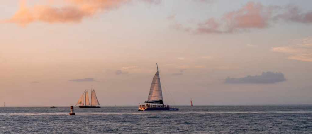 Sailboats crossing the ocean beneath a pink and orange sunset in Key West, Florida