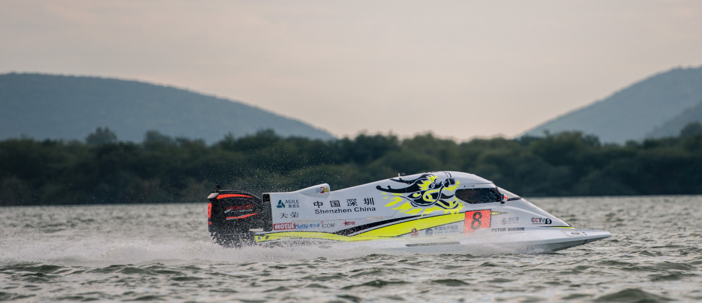White racing motorboat speeding across open water and creating a wide trail of spray