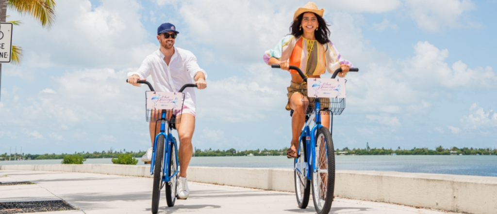 Couple riding Blue Flamingo bicycles along a palm-lined waterfront path in Key West